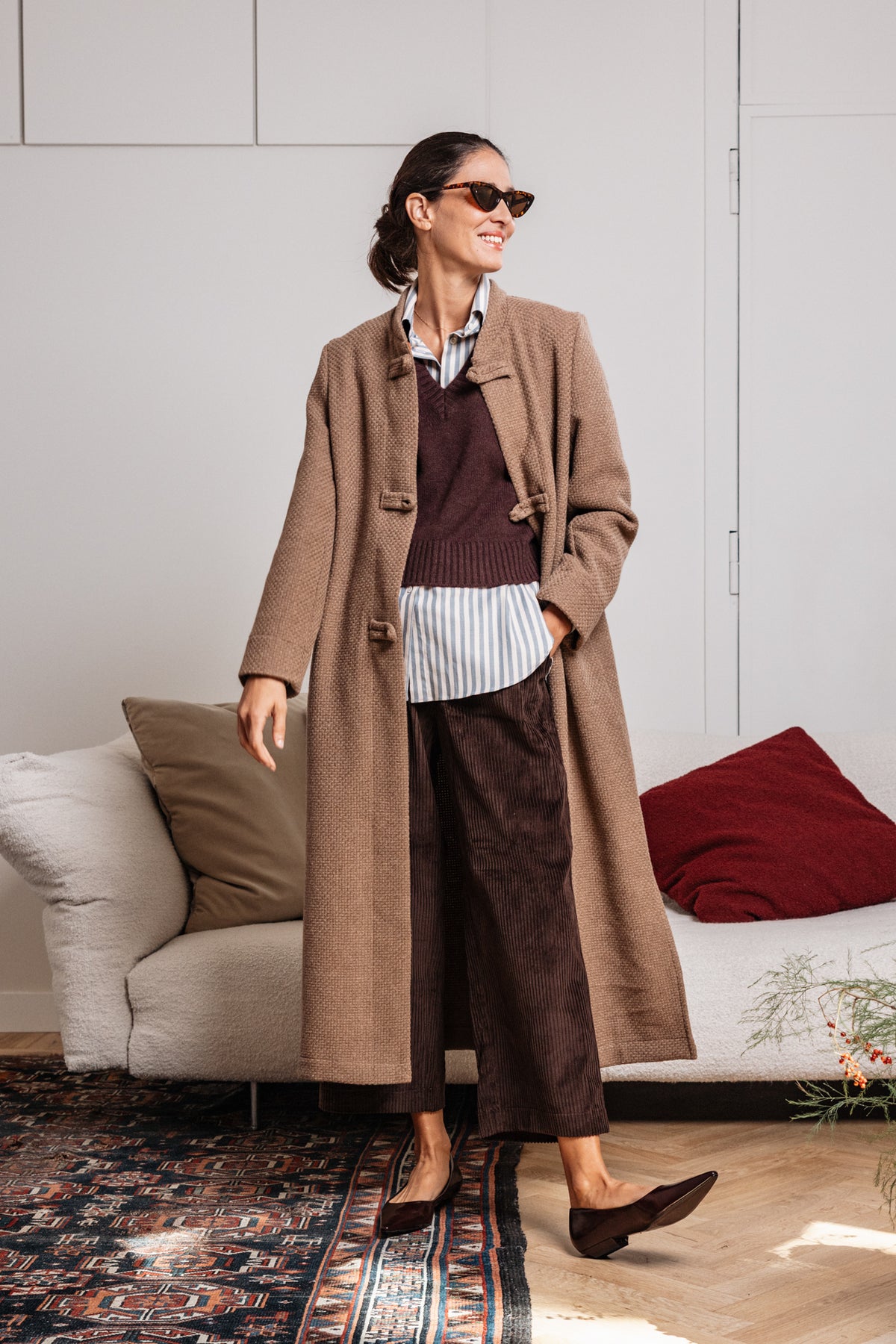 Cappotto lungo beige tortora da donna con alamari, indossato con pantaloni marroni in velluto – Paglia Milano.