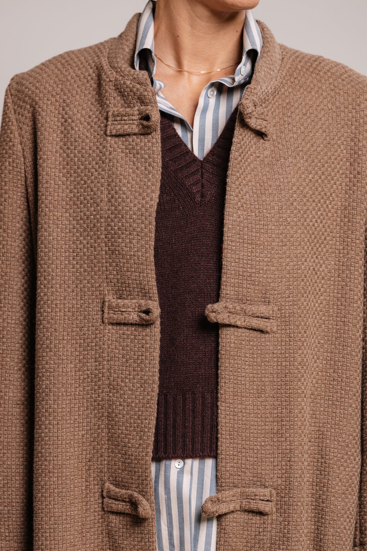 Cappotto beige tortora con chiusura ad alamari rivestiti in tessuto e spalle strutturate.