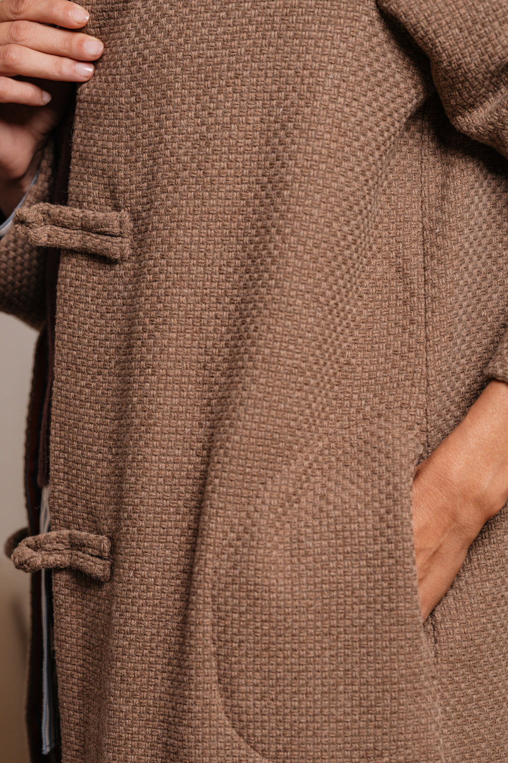 Primo piano della trama intrecciata beige e della tasca laterale del cappotto.