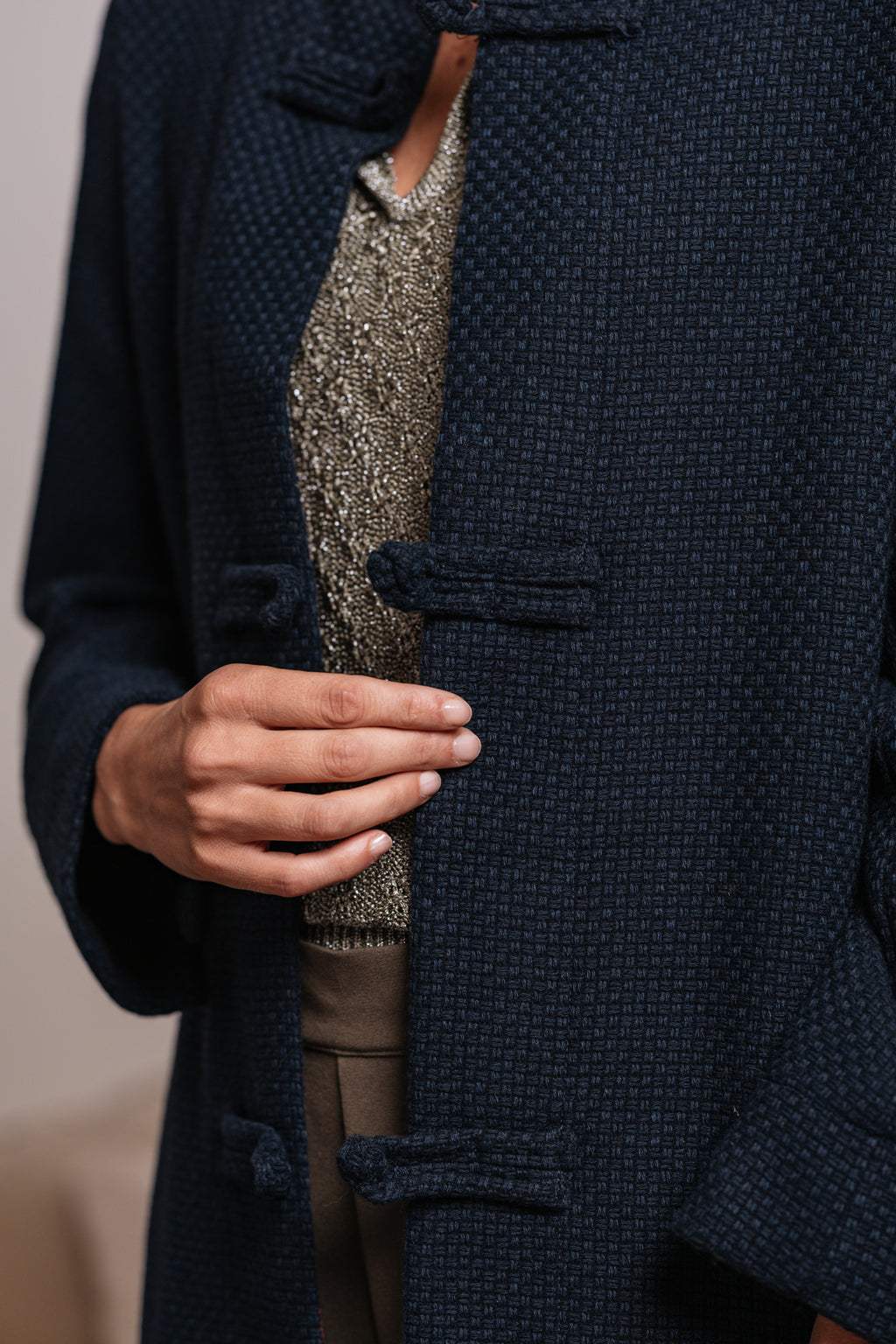 Cappotto blu con chiusura ad alamari in tessuto e spalle strutturate.