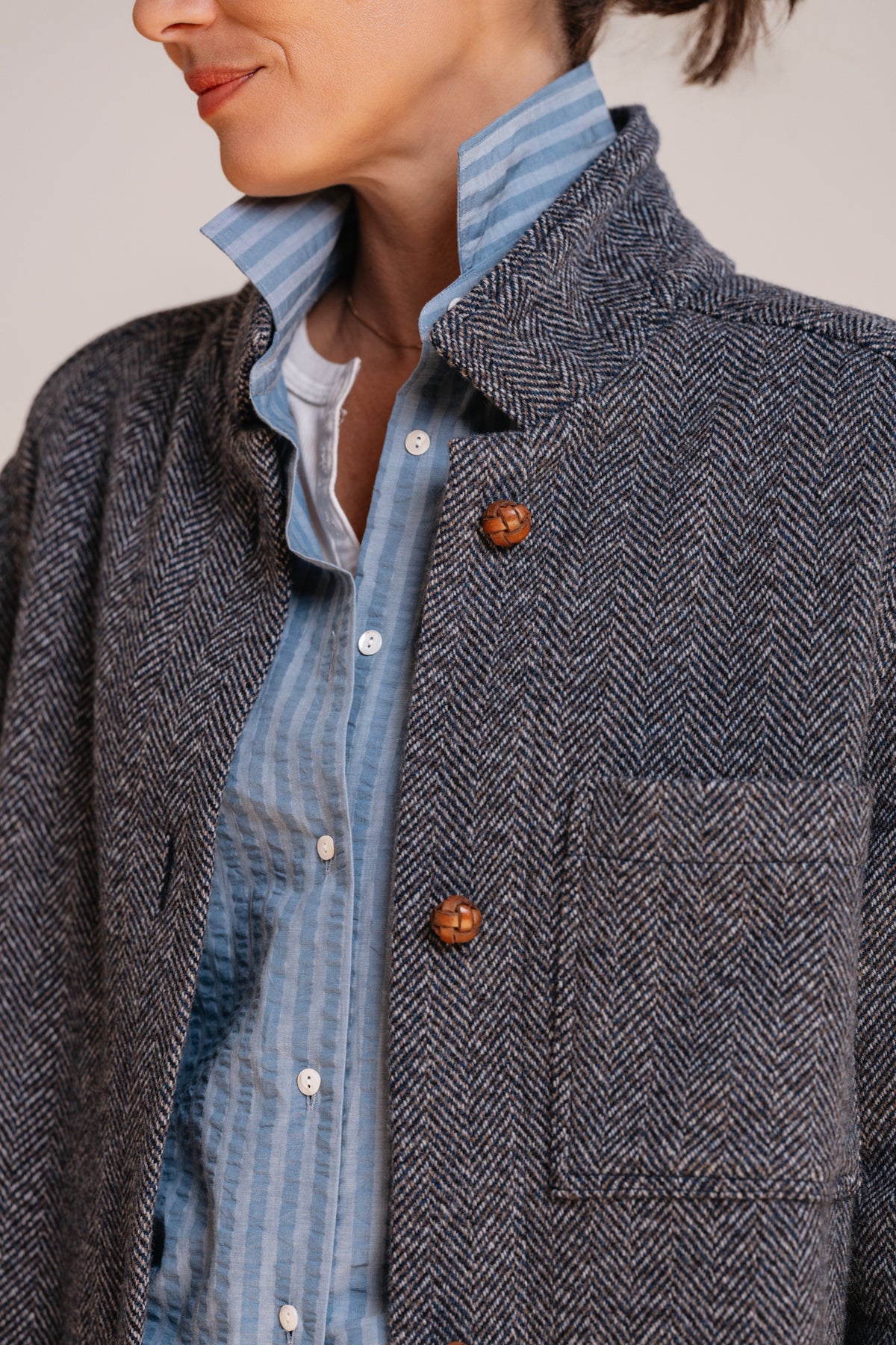 Dettaglio del tessuto blu spigato del cappotto ERNESTO, con collo sartoriale e bottoni in pelle intrecciata.